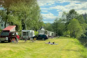 Campingwiese mit Wohnwagen und einem Fahrrad, daneben ein Auto und Liegen auf dem Rasen.