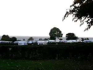 Wohnwagen auf einem Campingplatz zwischen Bäumen, im Hintergrund eine weite Stadtansicht.
