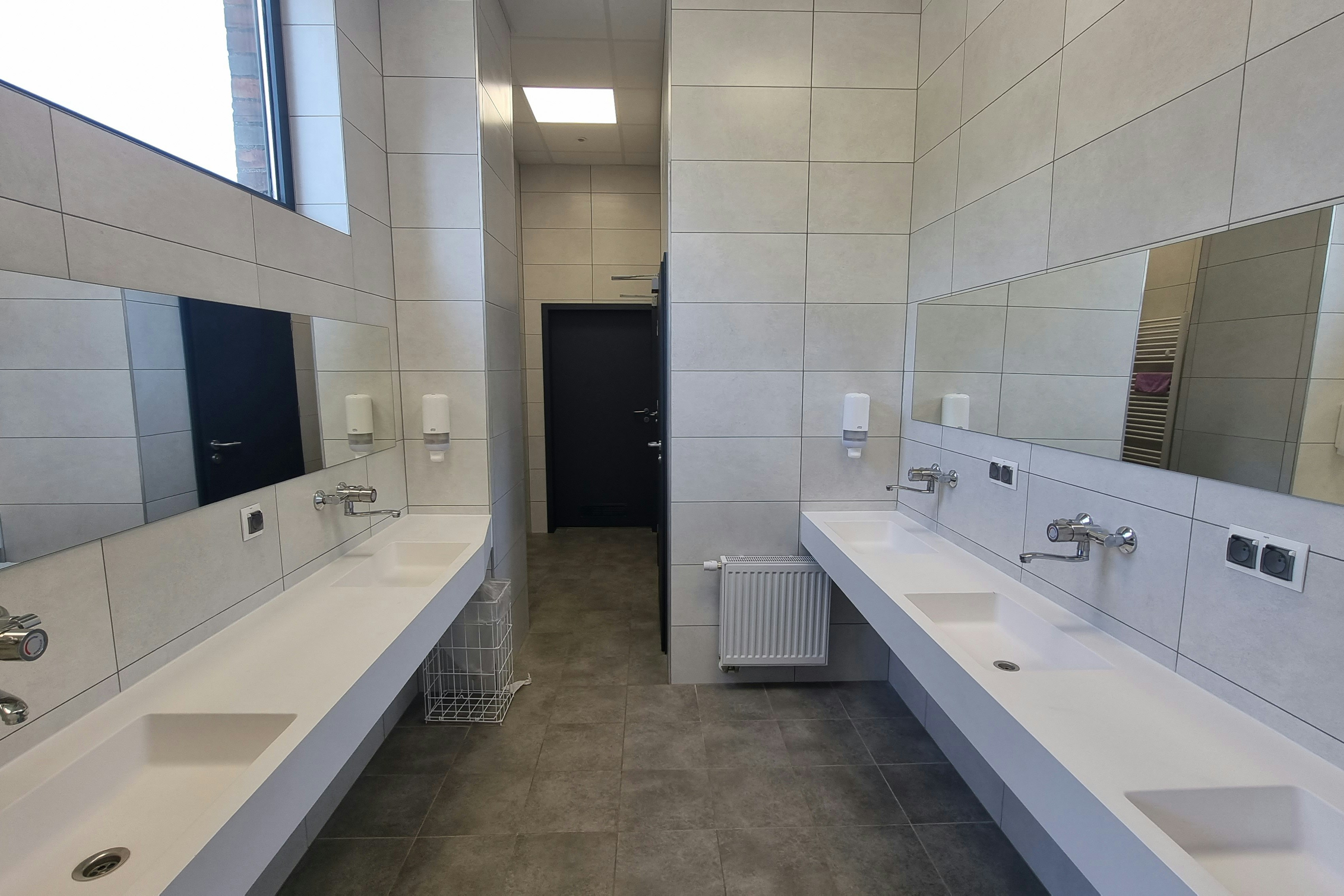Camping-Badezimmer mit zwei langen Waschtischen, Spiegeln, Wasserhähnen und Toiletten im Flur.
