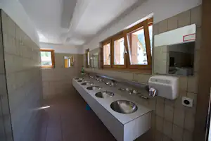 Waschraum im Campingbereich mit mehreren Waschbecken, Armaturen, Fliesenwänden und Fenstern in der Seitenwand.