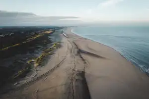 Küstenstraße entlang eines langen Sandstrands, Blick von oben auf die Kurve und das ruhige Meer.