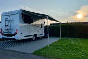 Weißes Wohnmobil auf Stellplatz mit ausgefahrener Markise, gepflasterter Fläche und Rasen am Abendhimmel.