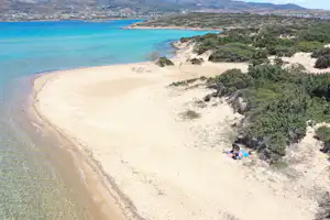 Weite Sandbucht am Meer mit türkisfarbenem Wasser, Dünen und bewachsenen Hängen entlang der Küste.