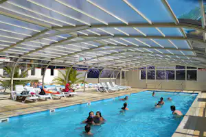 Überdachtes Schwimmbecken auf dem Campingplatz, Liegen unter dem Dach und mehrere Personen im Wasser.