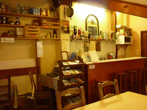 Campingbar mit Holztheke, Barhockern und Getränkeflaschen im Regal, daneben Schilder und Gläser an der Wand.