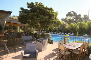 Terrasse mit Gartenmöbeln und Blick auf den Pool, umgeben von Bäumen und Sträuchern am Campingplatz.