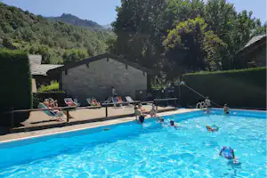 Großer Camping-Pool mit mehreren Liegen, Steinmauer und Bäumen im Hintergrund, umgeben von grünen Hügeln.