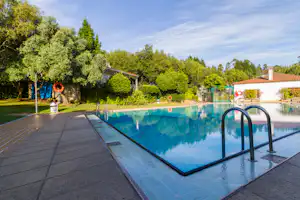 Schwimmbecken mit Treppenstufen und Edelstahlgeländer, umgeben von Terrasse und Bäumen am Campingplatz.
