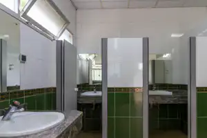 Badezimmer im Campingbereich mit Waschbecken, Armaturen und Dusche in hellen Fliesen, mehrere Kabinen mit Türen.