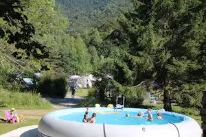 Aufblasbarer Pool auf dem Campingplatz im grünen Tal, Zelte im Hintergrund und Bäume entlang des Weges.
