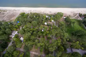Luftaufnahme eines Campingplatzes mit vielen Bäumen, Wegen und Stellplätzen nahe dem Seeufer.