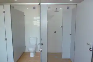 Badezimmer im Campingbereich mit mehreren Kabinen, weißen Toiletten und hellen Fliesen, Türen und Handtuchhaken an den Wänden.