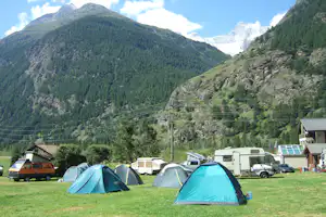 Campingplatz mit mehreren Zelten und Wohnmobilen, im Hintergrund grüne Berge und schneebedeckter Gletscher.