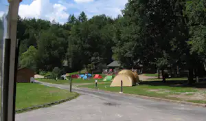 Zelt auf einem Campingplatz neben einem Weg, Rasenfläche und Bäumen im Hintergrund.