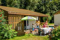 Camping Au Clos de la Chaume - Mobilheim mit überdachter Veranda, vor der eine Familie einen Esstisch deckt