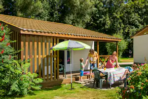 Camping Au Clos de la Chaume - Mobilheim mit überdachter Veranda, vor der eine Familie einen Esstisch deckt