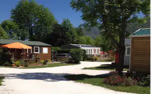 Reihe von Mobilheimen am Campingplatz, gepflasterter Weg, Rasen und Bäume im Hintergrund.