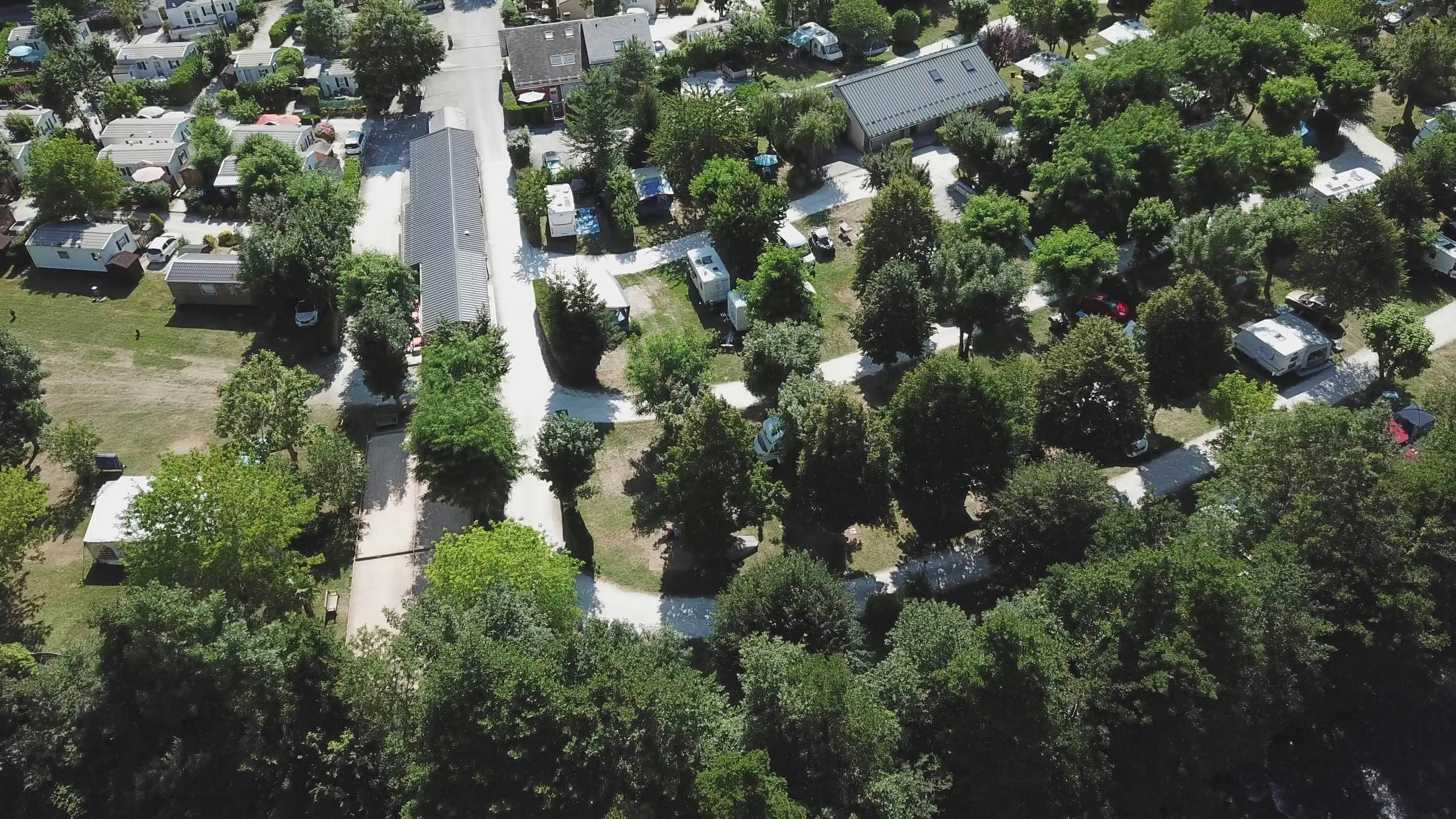 Luftaufnahme einer Campinganlage mit Wegen, Wohnwagen und kleinen Gebäuden zwischen Bäumen und gepflegten Grünflächen.