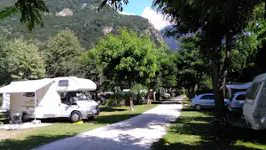 Wohnwagen und Campingfahrzeuge auf einem Stellplatz im Grünen, mit Bäumen und einem Weg zwischen den Fahrzeugen.