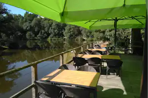 Grüne Markise über Terrasse mit Holztisch und Stühlen, Blick auf den See und Bäume am Ufer.