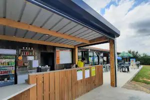 Holz-Rezeption mit Theke, Getränkekühlern und Stühlen im Außenbereich eines Campingplatzes.