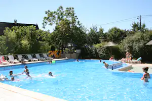 Schwimmbecken auf dem Campingplatz mit Sonnenschirmen, Liegestühlen und Bäumen im Hintergrund.