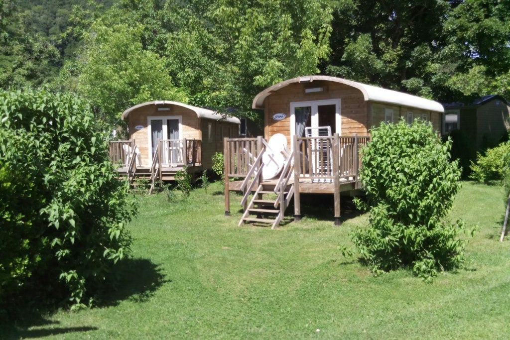 Zwei Mobilheime auf Holzpodesten mit Treppen, umgeben von Büschen und Rasen im Campingbereich.