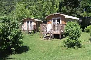 Zwei Mobilheime auf Holzpodesten mit Treppen, umgeben von Büschen und Rasen im Campingbereich.