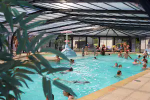 Überdachtes Schwimmbecken auf dem Campingplatz, viele Badegäste im Wasser, Liegen und Sitzbereiche im Hintergrund.