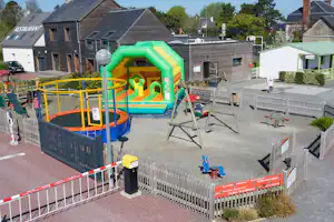 Spielplatz mit großer Hüpfburg auf einem Campingplatz, umgeben von Zäunen, Wohnwagen und Wohnhäusern im Hintergrund.