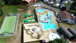 Luftaufnahme einer Campinganlage mit großen Schwimmbecken, Kinderbecken und Sportplatz, umgeben von Stellplätzen und Wegen.