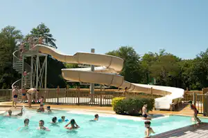 Wasserrutsche über dem Pool auf dem Campingplatz, Holzterrasse und Zaun, Kinder planschen im Becken.