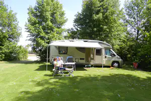 Wohnmobil mit ausgefahrenem Sonnendach auf dem Campingplatz, davor zwei Campingstühle und Tisch auf grünem Rasen.