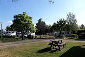 Wohnmobile auf dem Campingplatz zwischen Bäumen, mit Kiesweg und Picknicktisch im Vordergrund.