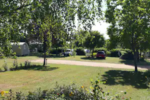 Campingstellplatz mit Wohnwagen und Zelten, Autos auf dem Weg, umgeben von Bäumen und Rasen.