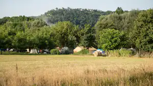 Campingwiese mit mehreren Zelten, umgeben von Bäumen und einem bewaldeten Hügel im Hintergrund.