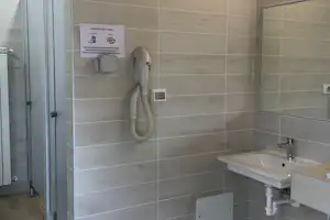 Camping-Badezimmer mit Waschbecken, Fliesenwand, Handtuchhalter und Wandgerät mit Schlauch.