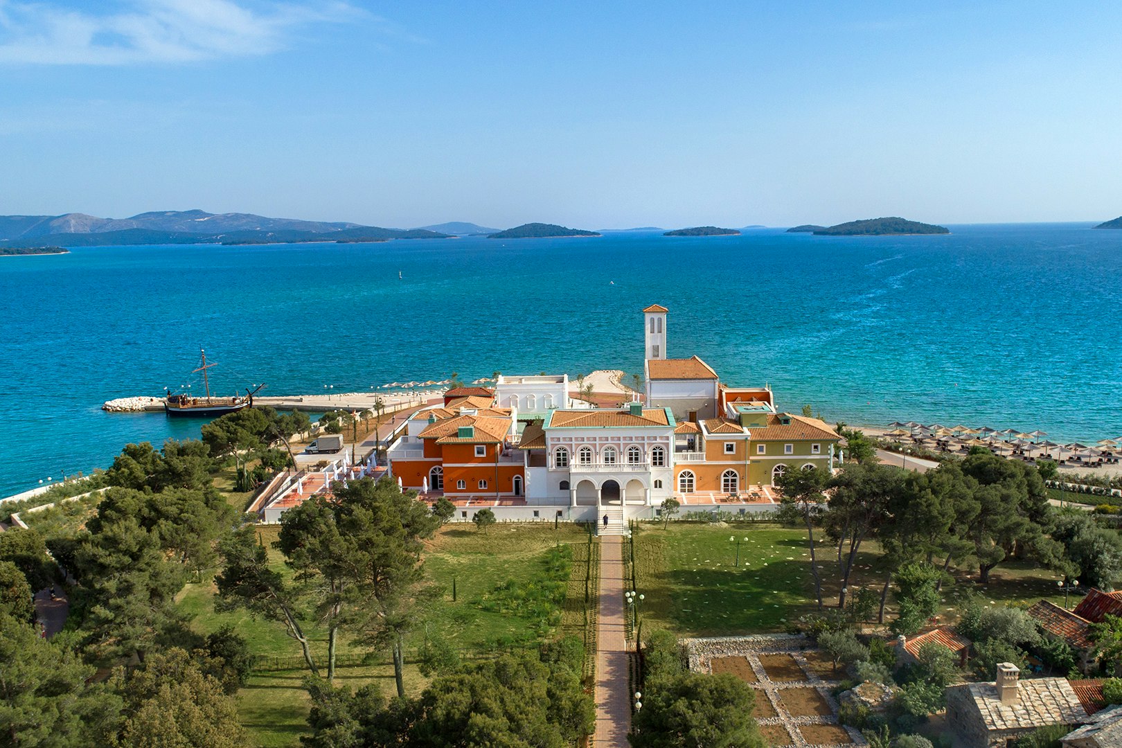 Campinganlage am Meer mit gepflegtem Garten, mehreren Gebäuden mit Terrassen und Blick auf den Strand und das Wasser.