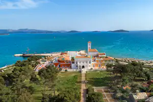 Campinganlage am Meer mit gepflegtem Garten, mehreren Gebäuden mit Terrassen und Blick auf den Strand und das Wasser.