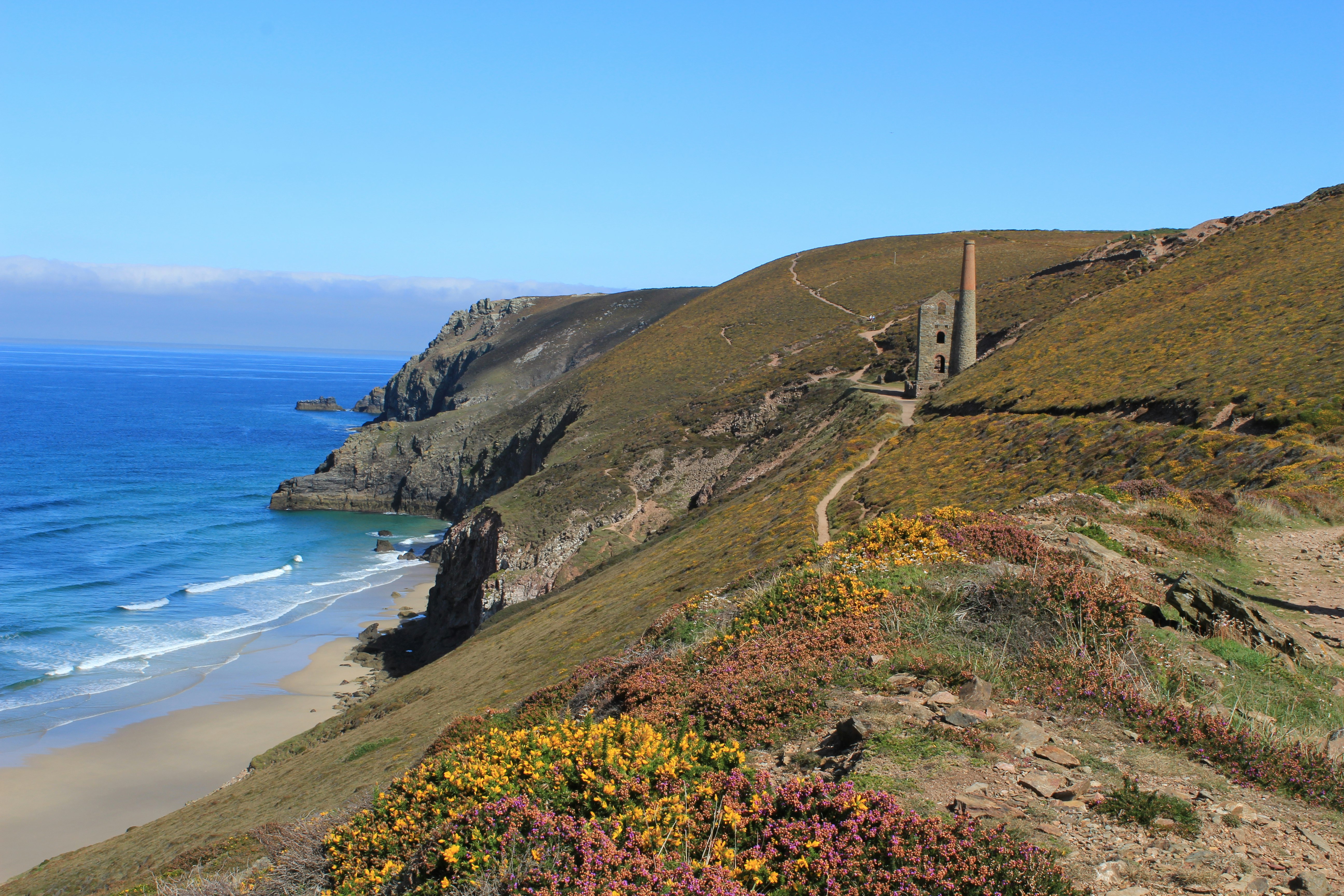 Beacon Cottage Farm Holidays - Blick auf die steile Küste mit bewachsenem sandig-felsigem Hang und einer Ruine, daneben der Übergang zum blauen Meer