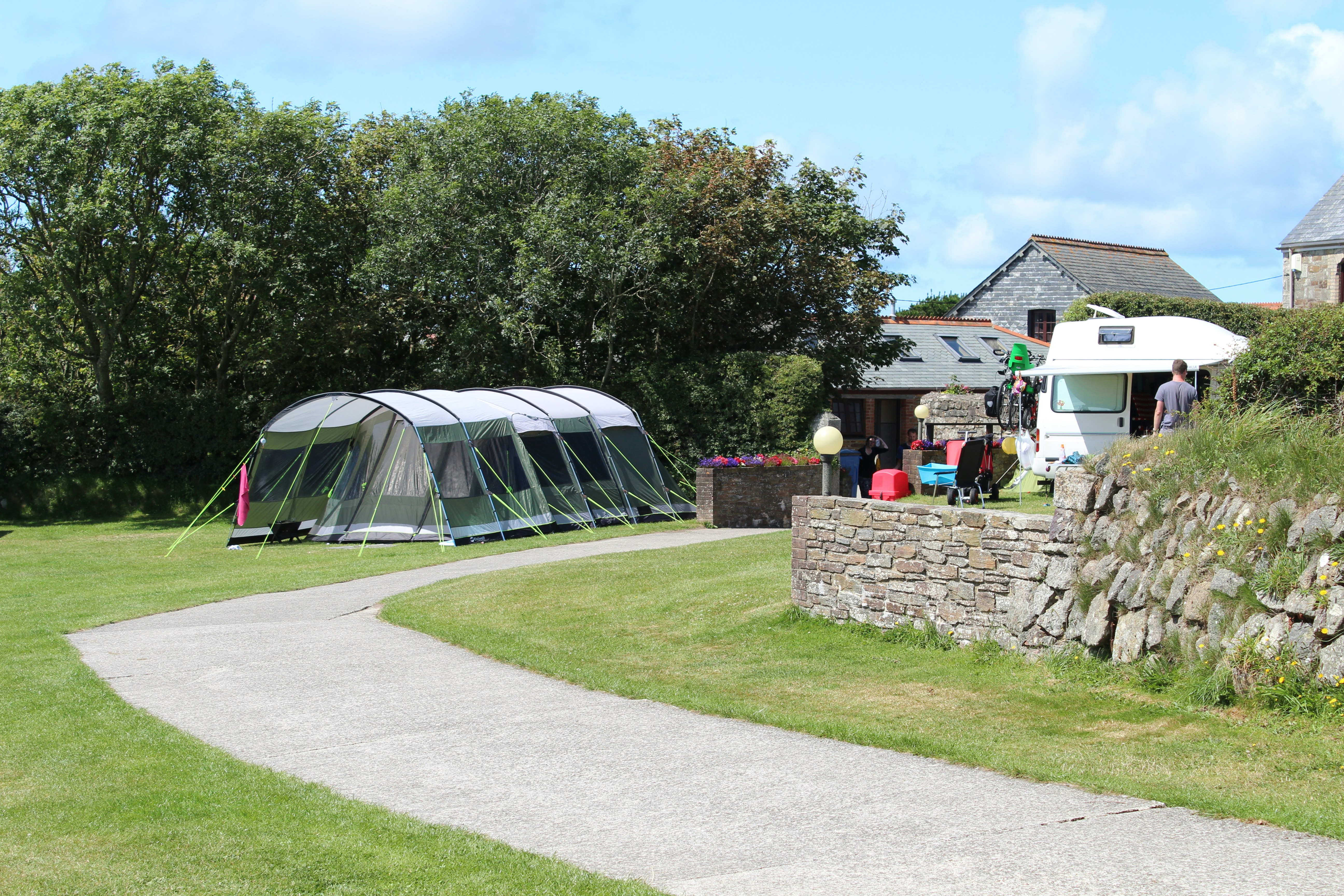 Beacon Cottage Farm Holidays - Zelt auf der Zeltwiese unter schattenspendenden Bäumen und ein Wohnmobil vor den Gebäuden des Campingplatzes