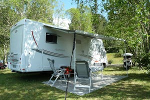 Wohnwagen im Grünen mit Vordach und Campingstühlen und Tisch auf dem Camping Beau Rivage