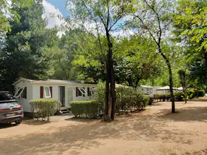 Reihen von Wohnwagen auf einem Campingplatz, mit Kiesweg, Büschen und Bäumen im Vordergrund.