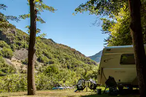 Wohnmobil auf dem Campingplatz zwischen Bäumen, im Hintergrund bewaldete Berge und ein sonniger Himmel.
