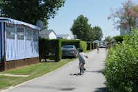 Camping Bel Air - Mobilheime auf dem begrünten Campingplatz und Kind auf Fahrrad