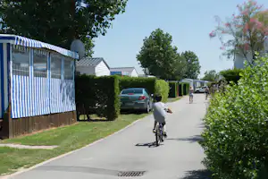Camping Bel Air - Mobilheime auf dem begrünten Campingplatz und Kind auf Fahrrad