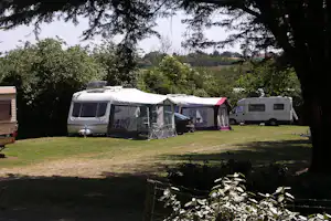 Wohnmobile mit Vorzelten auf einem Campingplatz, umgeben von Rasen und Büschen, im Hintergrund weitere Fahrzeuge.