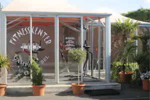 Überdachte Camping-Terrasse mit großen Schiebetüren, Fahrrädern und Topfpflanzen vor dem Gebäude.