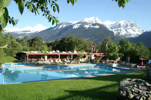 Camping Bella-Tola - Swimmingpoo mit Sonnenliegen und Liegewiese mit den Alpen im Hintergrund