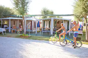 Campingstellplatz mit Zeltvorbau, Gartenstühlen und Wäscheleine, im Vordergrund fährt ein Fahrrad vorbei.